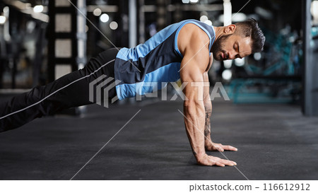 Sporty young man doing pushups in gym, side view, free space 116612912