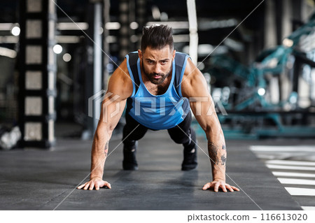 Concentrated muscular guy training in gym, doing push up exercises, free space 116613020