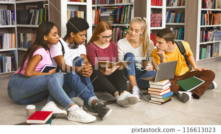 Group of diverse students sitting on floor at library in campus and studying, preparing for exams, free space 116613023