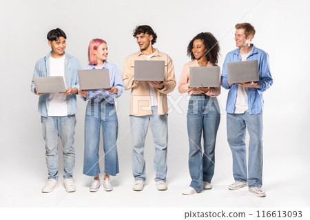 A group of five young adults, standing against a white background, hold open laptops in their hands. 116613093