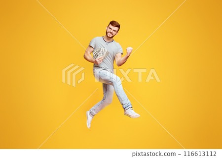 Celebrating Win. Lucky Young Man Jumping On Orange Studio Background With Money In His Hand, Gesturing Celebrating Win. Lucky Young Man Jumping On Orange Studio Background With Money In His Hand, Gesturing 116613112