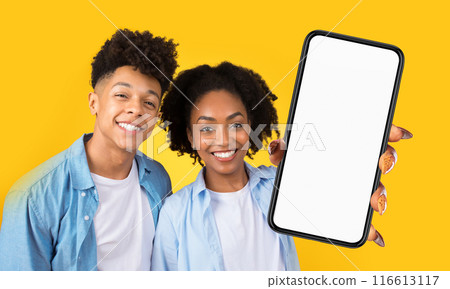 This image features a young African American man and woman, both smiling, with the woman holding up a smartphone with a blank screen. 116613117