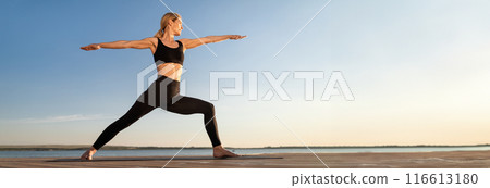 Beautiful Middle Aged Woman Practicing Yoga Outdoors, Standing In Warrior Pose On Fitness Mat, Sporty Female In Activewear Training On Wooden Pier Near Sea, Enjoying Healthy Lifestyle, Copy Space Beautiful Middle Aged Woman Practicing Yoga Outdoors, Standing In Warrior Pose On Fitness Mat, Sporty Female In Activewear Training On Wooden Pier Near Sea, Enjoying Healthy Lifestyle, Copy Space 116613180
