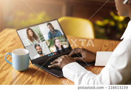 Black woman actively engaged with a laptop, with a group of people displayed on the screen. The individual appears focused and immersed in the digital interaction. Black woman actively engaged with a laptop, with a group of people displayed on the screen. The individual appears focused and immersed in the digital interaction. 116613239