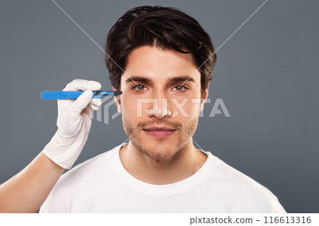 Cosmetic Operation. Portrait Of young man before plastic surgery, doctor hands with scalpel near patient's face 116613316