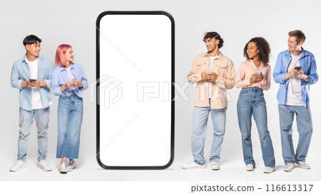 Multiracial people stand in front of a giant phone mockup with blank white screen. They are all looking at the phone and holding their own smartphones. 116613317