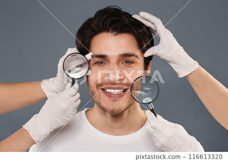 Beauty care and body modification. Beauticians examining young handsome man face through magnifiers 116613320