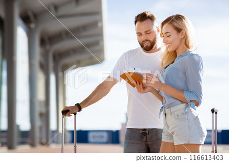 Traveling Together Concept. Two beautiful tourists looking at their documents standing ouside with luggage Traveling Together Concept. Two beautiful tourists looking at their documents standing ouside with luggage 116613403
