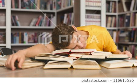 Sleeping at library. Tired caucasian guy having nap on books stack, being exhausted during preparing for exams 116613550