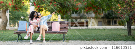 Two Happy Multiethnic Ladies Friends Relaxing On Bench After Shopping, Cheerful Young Women In Stylish Eyeglasses Resting Outdoors With Purchases After Walk In Summer City, Panorama, Copy Space Two Happy Multiethnic Ladies Friends Relaxing On Bench After Shopping, Cheerful Young Women In Stylish Eyeglasses Resting Outdoors With Purchases After Walk In Summer City, Panorama, Copy Space 116613551