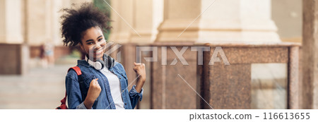 Cheerful African American Student Girl Celebrating Passed Exam Gesturing Yes Smiling To Camera Posing With Backpack Standing Outside Of College Building. I Did It, Educational Success, Copy Space Cheerful African American Student Girl Celebrating Passed Exam Gesturing Yes Smiling To Camera Posing With Backpack Standing Outside Of College Building. I Did It, Educational Success, Copy Space 116613655