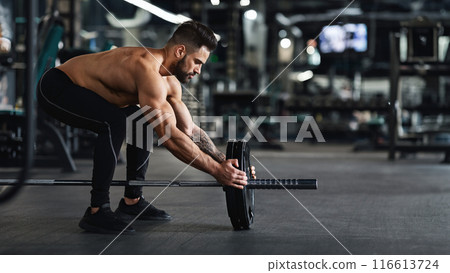 Athlete adding weight plates on his barbell, preparing for his weightlifting workout at gym, free space 116613724