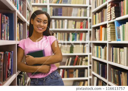 Education. Cheerful african american girl student standing at bookshelves in campus library, empty space Education. Cheerful african american girl student standing at bookshelves in campus library, empty space 116613757