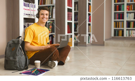 Creative caucasian student sitting on the floor with laptop at library, working on new project and listening to music, free space Creative caucasian student sitting on the floor with laptop at library, working on new project and listening to music, free space 116613763