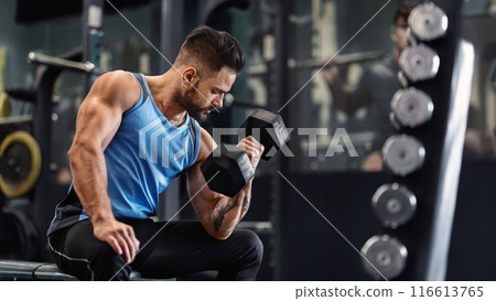 Bodybuilder pumping his biceps with dumbbell in gym, empty space Bodybuilder pumping his biceps with dumbbell in gym, empty space 116613765