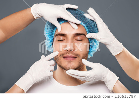Plastic surgery. Doctor's hands in gloves checking face of young man, closeup Plastic surgery. Doctor's hands in gloves checking face of young man, closeup 116613797