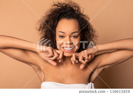 This image shows a smiling African American woman with curly hair. She is wearing a towel and is looking directly at the camera. Her expression is happy and carefree. 116613859