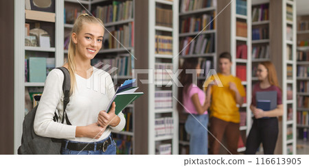 Educational process. Intelligent female student smiling at camera, library interior, free space Educational process. Intelligent female student smiling at camera, library interior, free space 116613905
