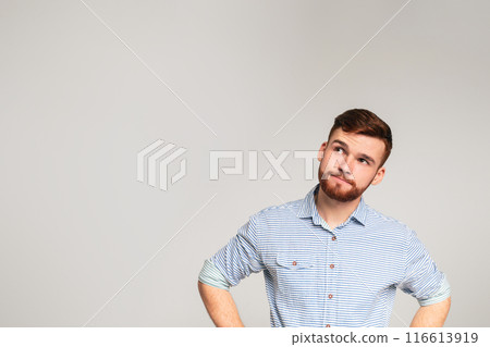 Thoughtful young bearded man wearing casual shirt looking away at copy space on grey studio background 116613919