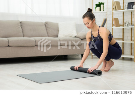 Rolling Mat After Practicing Yoga. Slim Woman Picking Fitness Equipment At Home Rolling Mat After Practicing Yoga. Slim Woman Picking Fitness Equipment At Home 116613976