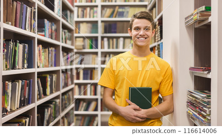 Knowledge. Cheerful caucasian male student standing between bookshelves in campus library, empty space Knowledge. Cheerful caucasian male student standing between bookshelves in campus library, empty space 116614006