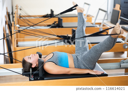 Girl in lying position is engaged in stretching muscles of legs and buttocks on simulator 116614021