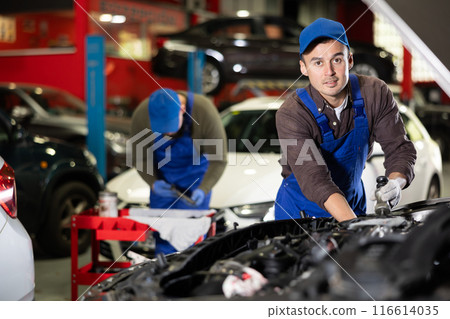 Skilled male auto mechanic in blue overalls repairing automobile Skilled male auto mechanic in blue overalls repairing automobile 116614035