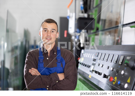 Portrait of positive man in blue overalls in window glass production workshop 116614119