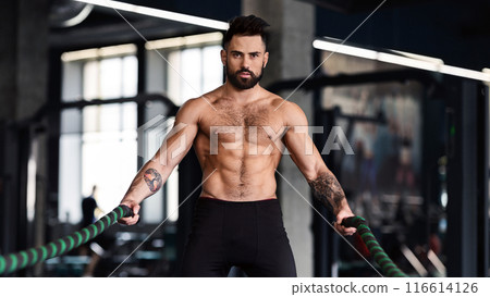 Muscular guy with naked torso exercising with battle ropes, crossfit training concept Muscular guy with naked torso exercising with battle ropes, crossfit training concept 116614126