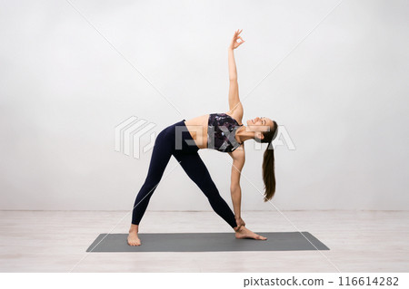 Woman Practicing Yoga Indoors, Making Revolved Triangle Pose, Light Brick Wall Woman Practicing Yoga Indoors, Making Revolved Triangle Pose, Light Brick Wall 116614282