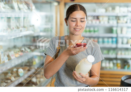 Young woman in supermarket scan QR code on bottle of milk Young woman in supermarket scan QR code on bottle of milk 116614317