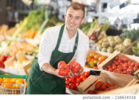 Man supermarket worker with some tomatoes in hands examines product Man supermarket worker with some tomatoes in hands examines product 116614318