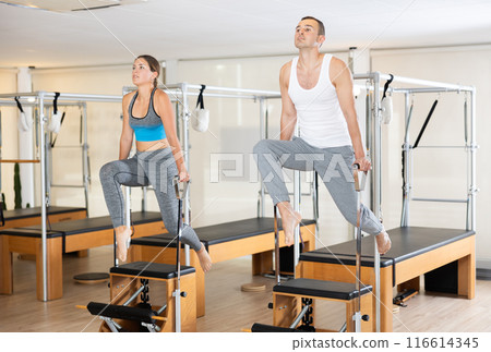 Sporty couple practicing Pilates on wunda chairs in fitness studio 116614345