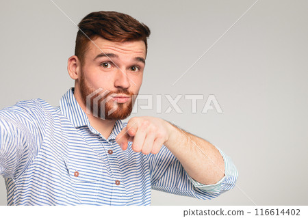 You are cool. Young bearded guy making selfie and pointing you with finger against grey studio background 116614402