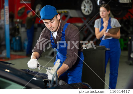 Young guy mechanic repairs car in car service station 116614417