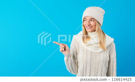 A woman wearing a white sweater and hat points at something off-camera, her body language indicating excitement or curiosity. Her outfit contrasts starkly against the background. A woman wearing a white sweater and hat points at something off-camera, her body language indicating excitement or curiosity. Her outfit contrasts starkly against the background. 116614425