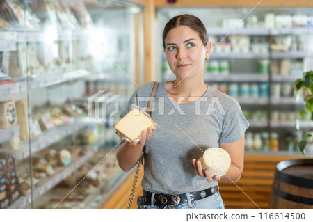 Positive young girl purchaser choosing cheese in large supermarket Positive young girl purchaser choosing cheese in large supermarket 116614500