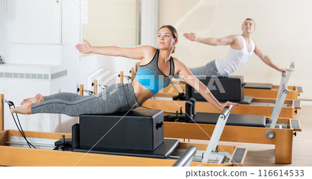 Concentrated girl practicing exercises on Pilates reformer with sitting box 116614533