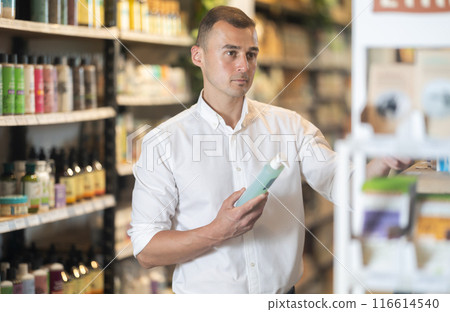 Thoughtful young man purchaser choosing cosmetic product in large supermarket 116614540