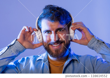 A bearded man wearing headphones listening to music or audio content. He is likely engaged in activities such as walking, working, or relaxing while enjoying the sound through his headphones. A bearded man wearing headphones listening to music or audio content. He is likely engaged in activities such as walking, working, or relaxing while enjoying the sound through his headphones. 116614552