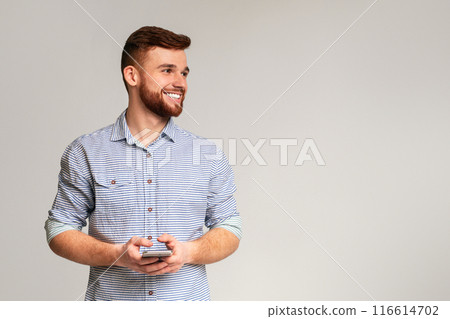 Young man blogger using his phone and looking away on copy space, isolated on grey studio background Young man blogger using his phone and looking away on copy space, isolated on grey studio background 116614702