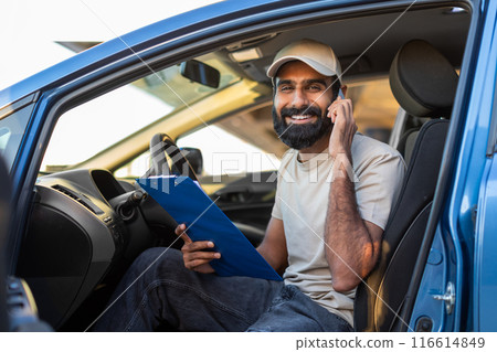 Indian man is seated in the drivers seat of a car, engaged in a phone conversation. He holds a cell phone to his ear, with a focused expression on his face Indian man is seated in the drivers seat of a car, engaged in a phone conversation. He holds a cell phone to his ear, with a focused expression on his face 116614849