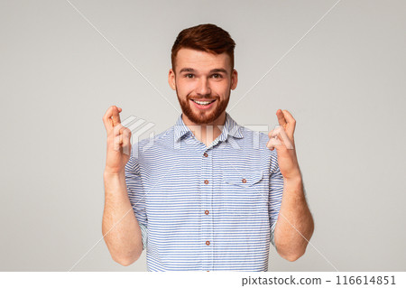 Positive millennial bearded stylish guy crossing fingers and making wish on beige studio background Positive millennial bearded stylish guy crossing fingers and making wish on beige studio background 116614851