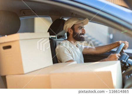 A cheerful Indian delivery driver is seen inside a car, surrounded by packages. He is smiling as he drives through a residential neighborhood on a sunny day A cheerful Indian delivery driver is seen inside a car, surrounded by packages. He is smiling as he drives through a residential neighborhood on a sunny day 116614865