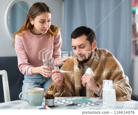 Man with viral disease sitting at home table with worried wife Man with viral disease sitting at home table with worried wife 116614876