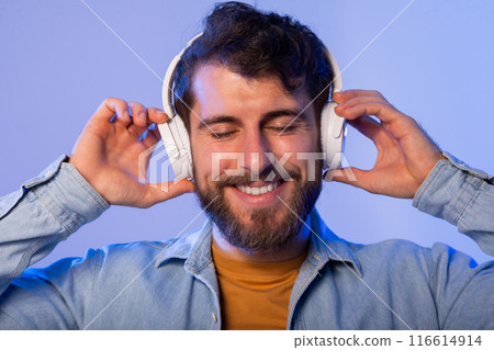 A man is shown wearing headphones and smiling directly at the camera. He appears happy and engaged, exuding a sense of enjoyment and contentment. 116614914