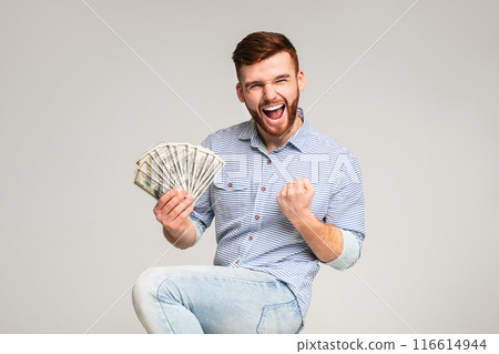 Win a lottery. Young handsome guy happy to have fan of dollars in hand, grey studio background, free space Win a lottery. Young handsome guy happy to have fan of dollars in hand, grey studio background, free space 116614944