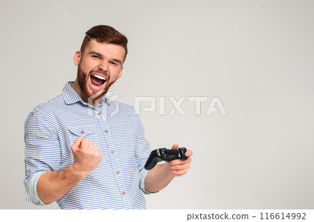 Victory taste. Young bearded guy win video game and feel happy on grey studio background, free space 116614992