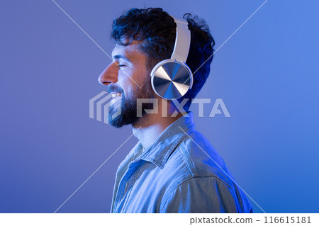A man with a beard is wearing headphones, immersed in listening to music. He appears focused on the sound, with a serious expression on his face. 116615181