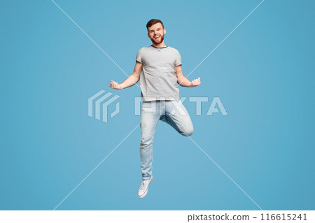 Celebrating Success. Excited Young Millennial Redhaired Man Jumping And Gesturing On Blue Studio Background 116615241